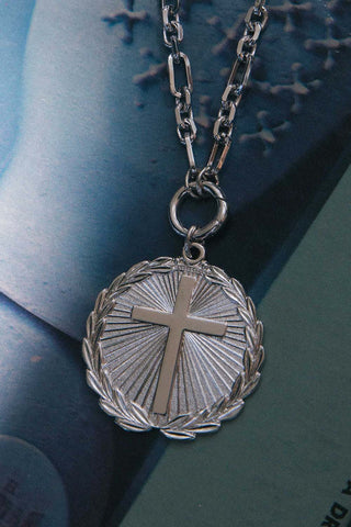 Silver necklace with a cross pendant on a textured surface