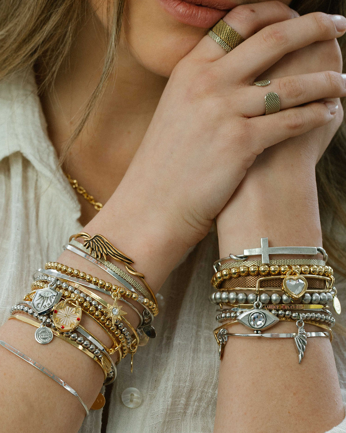 Close-up of a person's hands wearing multiple gold and silver bracelets with various charms.