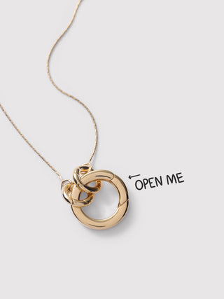 A gold necklace with a pendant made of two interlocking open rings, shown on a light gray background with the text 'OPEN ME' and an arrow pointing to the pendant.