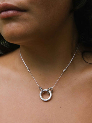 A close-up of a person wearing a delicate silver necklace with a small open ring pendant and tiny bead accents on the chain.