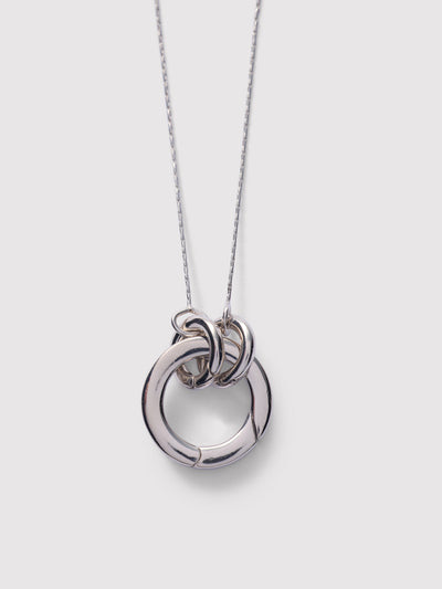 A silver pendant necklace featuring three interlocking circular rings on a delicate silver chain, set against a solid light gray background.