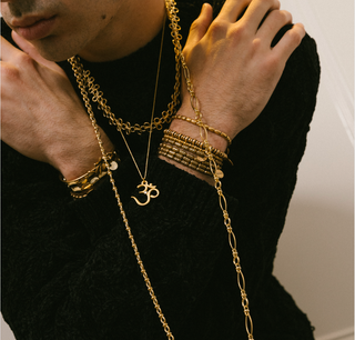 Close-up of a person wearing multiple gold necklaces and bracelets on a black sweater.